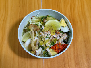 A bowl of Indonesian chicken soto with shredded chicken, sliced boiled egg, vermicelli, sliced...