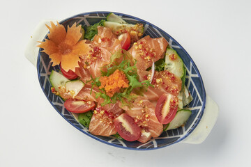 Fresh salmon sashimi salad served in decorative bowl with mixed greens, cherry tomatoes, cucumber slices, and spicy dressing, garnished with fish roe and carved carrot flower