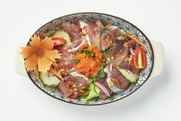 Fresh sashimi salad with raw fish slices, vegetables, and tobiko garnished with decorative carrot carving, served in patterned oval dish