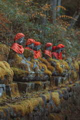 Moss-covered Jizo statues wearing red bibs and caps, lined along a forest path, symbolizing protection and peace. Nikko, Japan