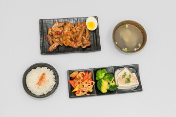 A savory beef rice bowl served as a set meal, featuring tender slices of beef simmered in soy-based sauce atop steamed white rice. The dish is accompanied by a variety of side vegetables and a light