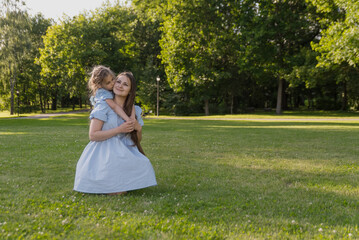 A daughter in a blue dress hugs and kisses her mother in sunlight on the right side of the text. A...