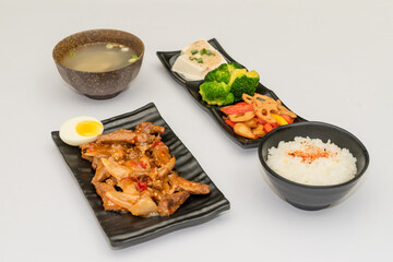 A savory beef rice bowl served as a set meal, featuring tender slices of beef simmered in soy-based sauce atop steamed white rice. The dish is accompanied by a variety of side vegetables and a light