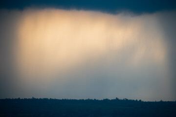 Dramatic Indian landscape photography featuring a rain-filled sky over a dark horizon line of trees.