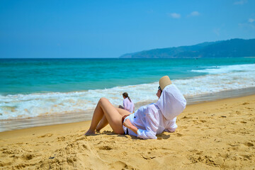 a girl is sitting on a sandy beach, looking at the sea
