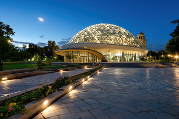Stunning architectural perspective of modern dome structure at dusk, surrounded by greenery and illuminated pathways