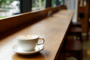 Cup of hot milk latte coffee on table by the window.