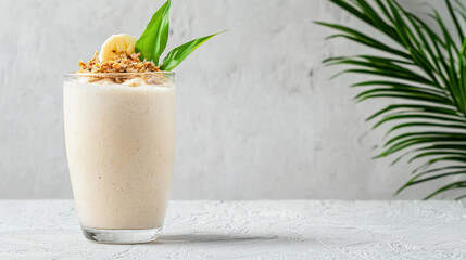 Refreshing banana smoothie topped with granola and slice of banana, surrounded by green leaves, evokes healthy lifestyle