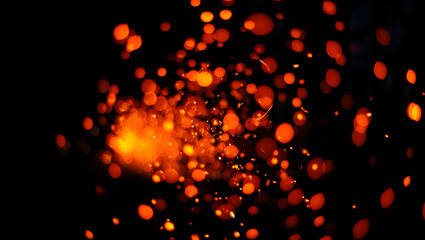 A burst of fiery orange sparks creates a mesmerizing bokeh effect in the dark