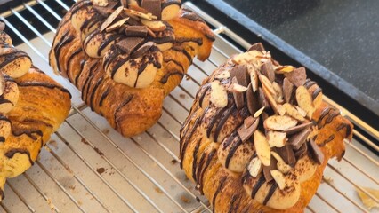 Flaky danish pastries topped with sliced almonds and dark chocolate drizzle on a cooling rack.
