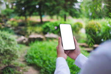 Mockup image of a woman holding mobile phone with blank white desktop screen in the nature outdoors