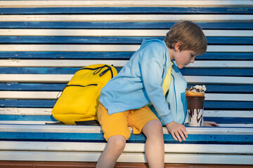Boy, child, schoolboy, sits thoughtfully, looks at ice cream.