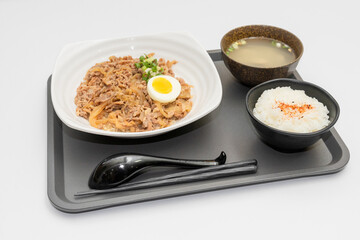 A savory beef rice bowl served as a set meal, featuring tender slices of beef simmered in soy-based sauce atop steamed white rice. The dish is accompanied by a variety of side vegetables and a light