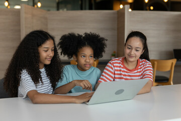 Diverse group of kids three girls happy looking at computer screen together, modern workspace. They...