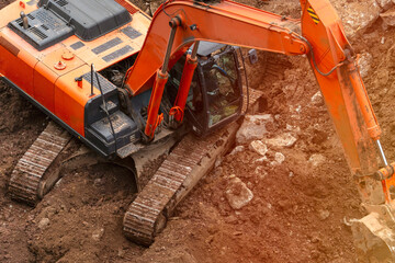 A large orange excavator is digging in the dirt. The machine is large and powerful, and it is clear that it is being used for a heavy-duty task. Concept of strength and determination