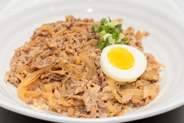A savory beef rice bowl served as a set meal, featuring tender slices of beef simmered in soy-based sauce atop steamed white rice. The dish is accompanied by a variety of side vegetables and a light
