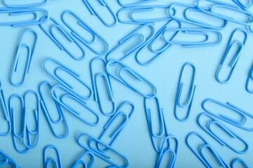 Many blue paper clips isolated on light blue background, flat lay