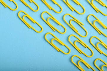 Many yellow paper clips isolated on light blue background, flat lay