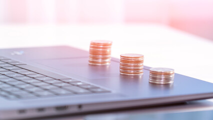 Three stacks of coins sit on top of a laptop keyboard. The coins are of varying sizes and are piled on top of each other. Concept of wealth and abundance