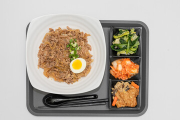 A Thai basil minced pork set meal arranged on a tray, including a portion of stir-fried spicy basil pork, a bowl of steamed white rice, three side vegetables, and a bowl of soup. The presentation refl