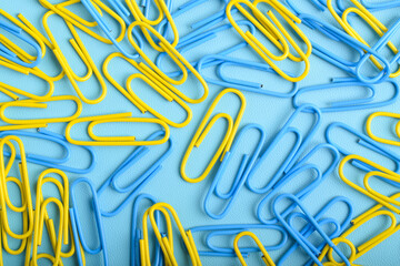Many yellow and blue paper clips isolated on light blue background, flat lay