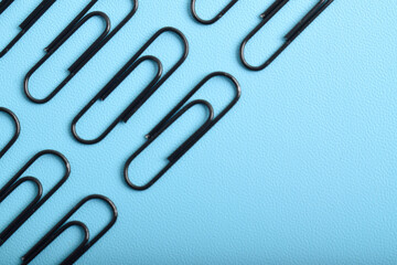 Many black paper clips isolated on light blue background, flat lay