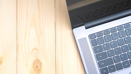 A laptop is on a wooden table. The laptop is open and the keyboard is visible. The table is made of wood and has a natural, rustic look