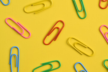 Colorful paper clips isolated on yellow background, flat lay, top view