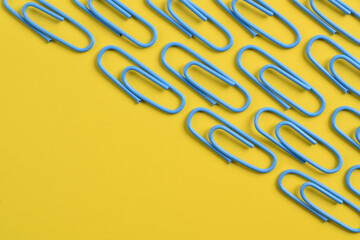 Many blue paper clips isolated on yellow background, flat lay
