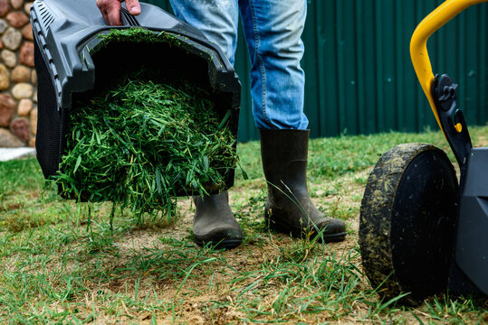 Man unloads mowed grass from a lawn's mower catcher into a wheelbarrow.