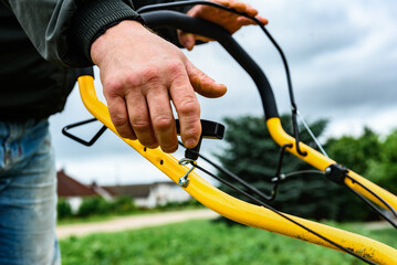 A man starts the engine of a petrol lawn mower with a starter rope. Mowing grass in summer.