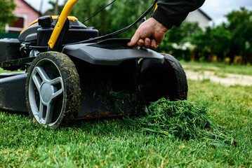 Man unloads mowed grass from a lawn's mower catcher into a wheelbarrow.