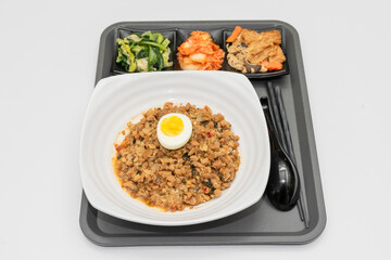 A Thai basil minced pork set meal arranged on a tray, including a portion of stir-fried spicy basil pork, a bowl of steamed white rice, three side vegetables, and a bowl of soup. The presentation refl