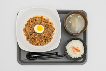A Thai basil minced pork set meal arranged on a tray, including a portion of stir-fried spicy basil pork, a bowl of steamed white rice, three side vegetables, and a bowl of soup. The presentation refl