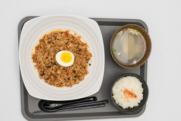 A Thai basil minced pork set meal arranged on a tray, including a portion of stir-fried spicy basil pork, a bowl of steamed white rice, three side vegetables, and a bowl of soup. The presentation refl