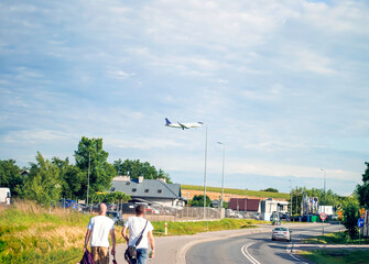 Airplane landing. Tourists watch the aircraft descend. Two men walk along the sidewalk against the backdrop of a flying plane