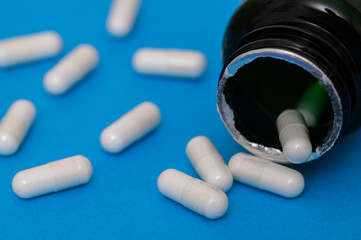 Oblong capsules with white powder spill out of the bottle