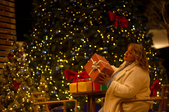 Plus size woman walks around the city during the Christmas of the week with a hot drink in a glass against the background of flickering light bulbs