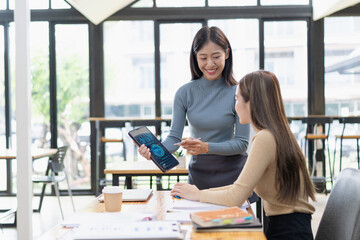 Two asian Businesswoman using tablet and laptop reviewing digital financial graphs and reports working in office desk.