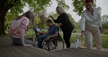 Friends share a relaxed day in a park, demonstrating true inclusivity and support. A person in a wheelchair is part of this joyful gathering, highlighting themes of companionship and accessibility.