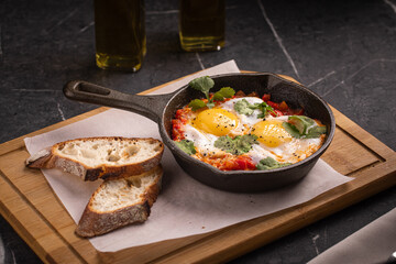 Shakshuka with poached eggs and vegetables served in skillet with bread