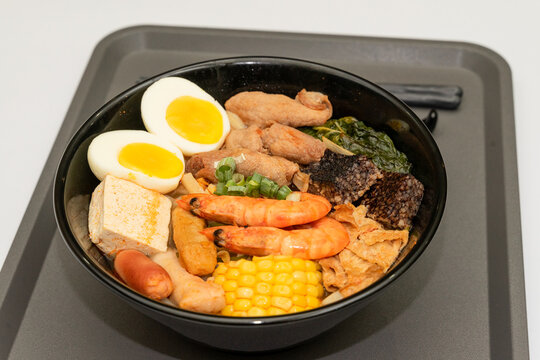 A hearty bowl of seafood noodle soup filled with shrimp, corn, egg, vegetables, rice blood cake, tofu skin, and assorted hotpot ingredients. The colorful ingredients float in a rich broth, making for 