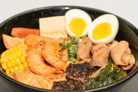 A hearty bowl of seafood noodle soup filled with shrimp, corn, egg, vegetables, rice blood cake, tofu skin, and assorted hotpot ingredients. The colorful ingredients float in a rich broth, making for 