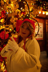 Plus size woman walks around the city during the Christmas of the week with a hot drink in a glass against the background of flickering light bulbs