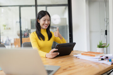 Happy young Asian businesswoman using digital tablet sitting in office.