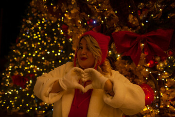 Plus size woman walks around the city during the Christmas of the week with a hot drink in a glass against the background of flickering light bulbs