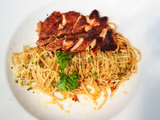 A mouth-watering plate of spaghetti aglio olio served with perfectly grilled chicken breast, topped with grated cheese and garnished with fresh parsley