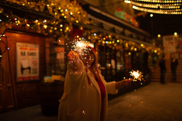 Plus size woman walks around the city during the Christmas of the week with a hot drink in a glass against the background of flickering light bulbs