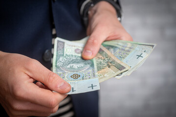 Elegant man counting Polish 100 zloty banknotes. Wealth, finance, and personal success concept. Close-up of male hands holding money in formal setting