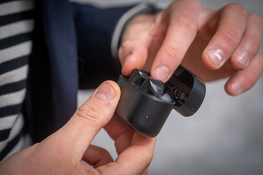 Man taking wireless earbuds out of charging case. Modern technology and lifestyle concept. Close-up of male hands using portable audio device